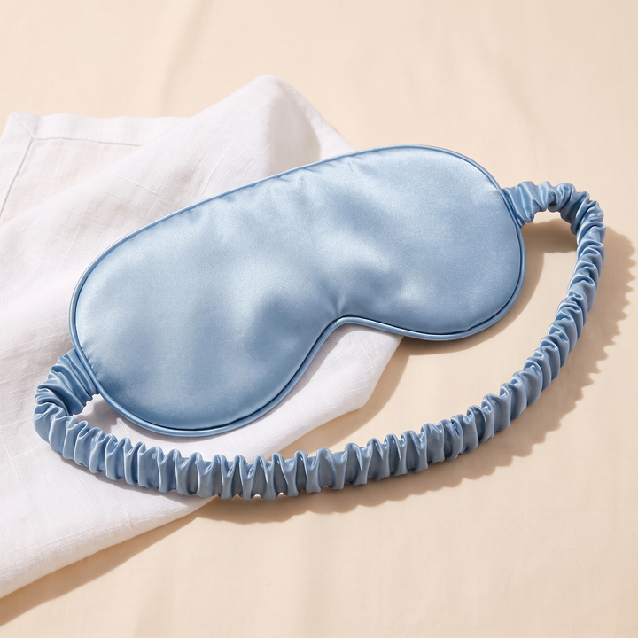 Silk Sleep Mask in Light Blue – half on a folded white napkin, strap looping toward camera
