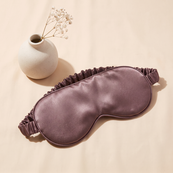 Silk Sleep Mask in Mauve – beside a speckled ceramic vase with dried baby&