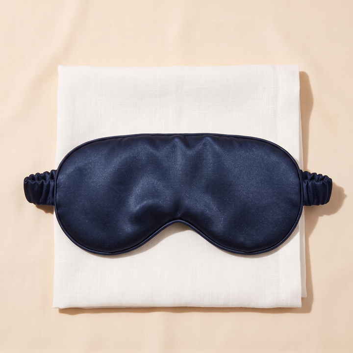 Silk Sleep Mask in Navy Blue – centered on a folded cream linen cloth, shot straight above