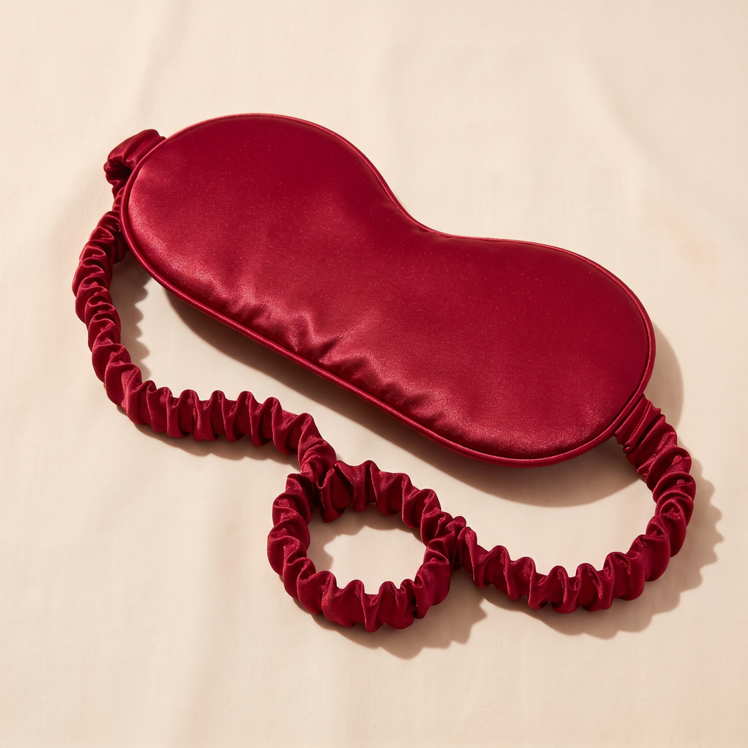 Silk Sleep Mask in Red – angled on cream fabric with strap curled into a loop
