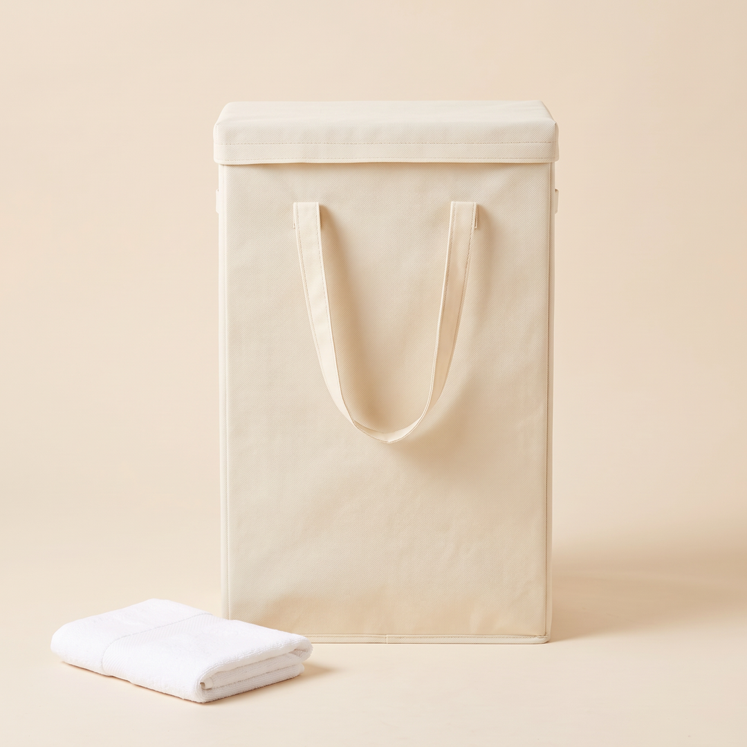 Slim Laundry Basket with Lid in Cream – front view with lid on, handles up, beside a folded white towel