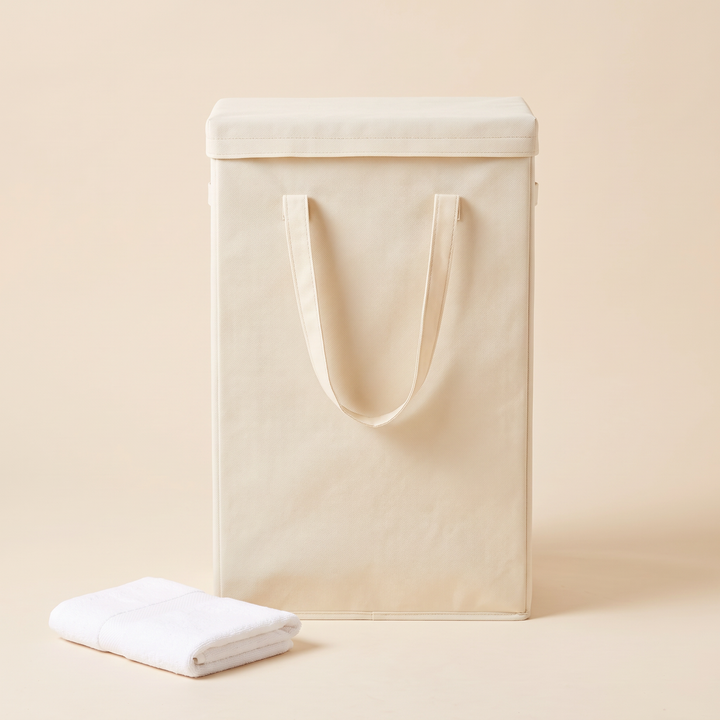 Slim Laundry Basket with Lid in Cream – front view with lid on, handles up, beside a folded white towel