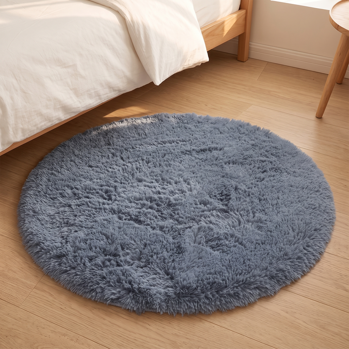 Small Round Shag Rug in Slate Blue – beside a white duvet and wooden bed frame in sunlight