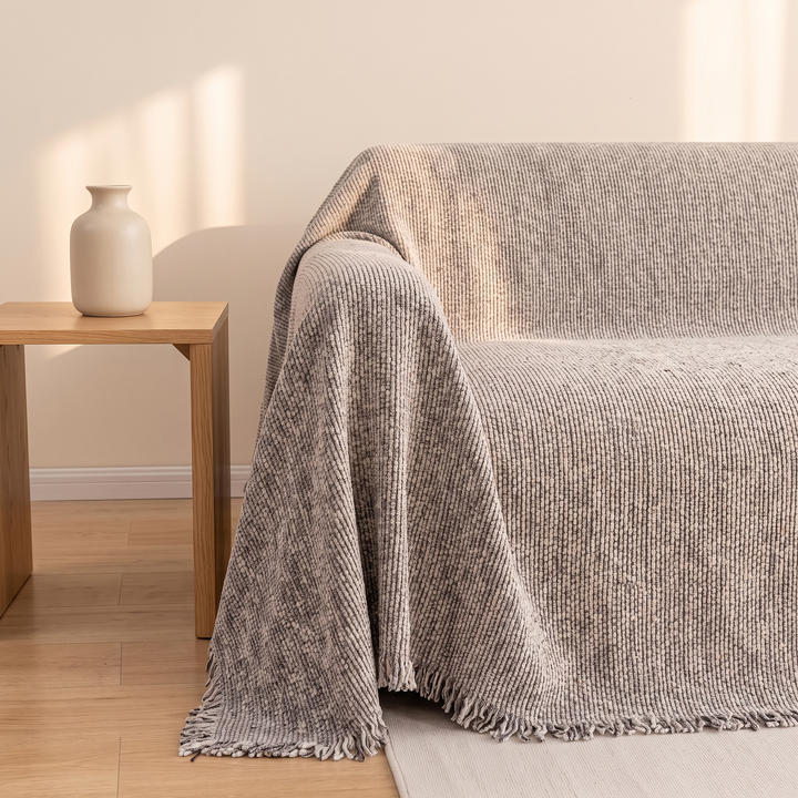 Speckled Chenille Couch Cover with Fringe in Oatmeal – side view over sofa arm beside wooden table with vase