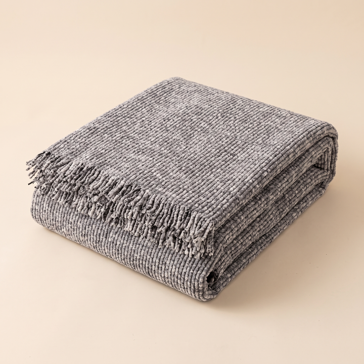 Speckled Chenille Couch Cover with Fringe in Gray – folded neatly into a stack against a plain beige backdrop