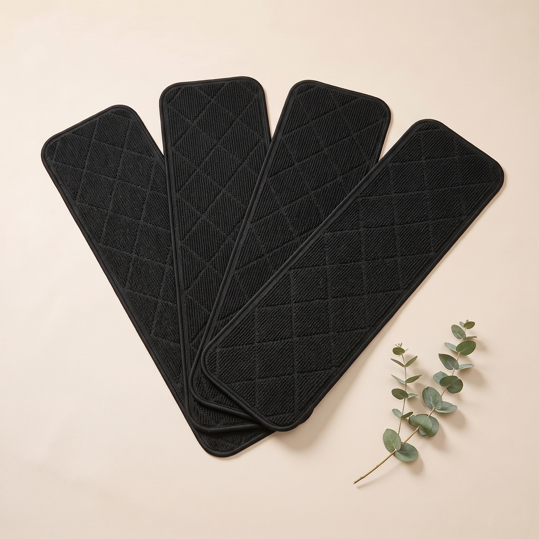 Carpet Stair Treads – Non-Slip, Self-Adhesive in Black – four treads fanned out overlapping beside a eucalyptus sprig on cream