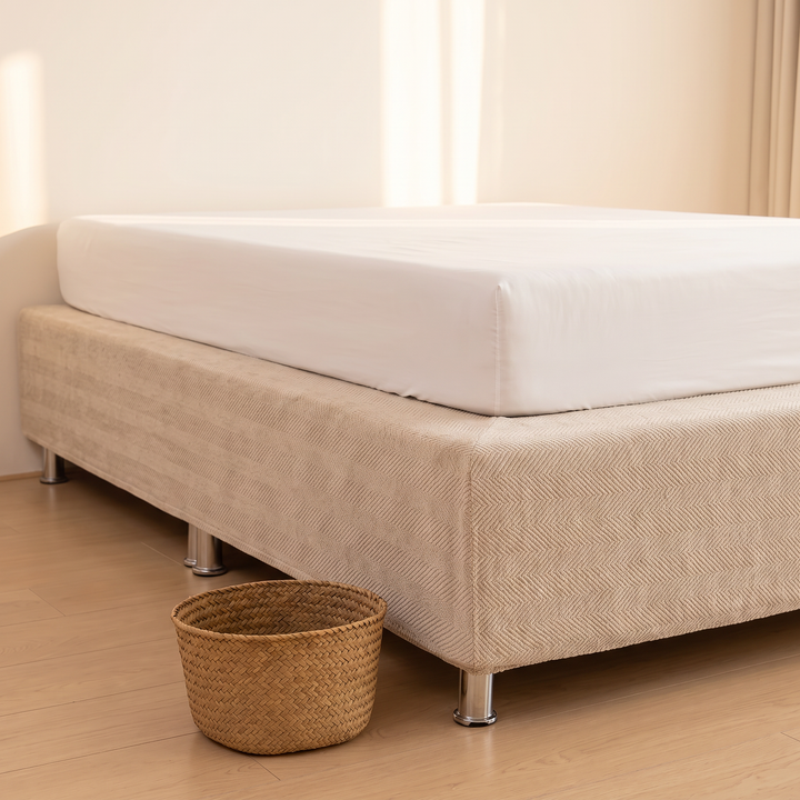 Stretch Box Spring Cover in Beige – low angle showing metal legs beside a woven basket