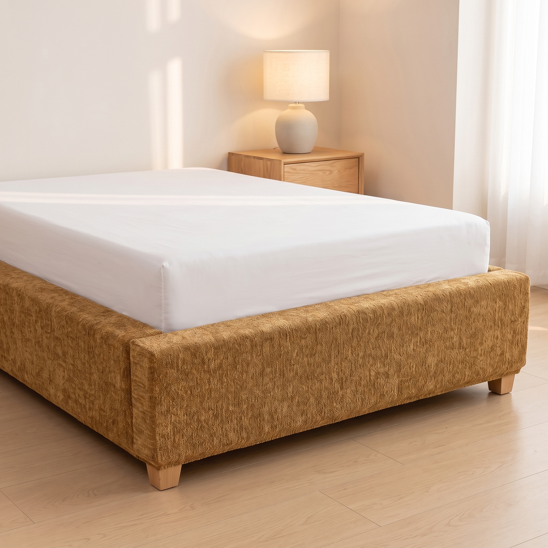 Stretch Box Spring Cover in Caramel – side panel and wooden feet with lamp in background