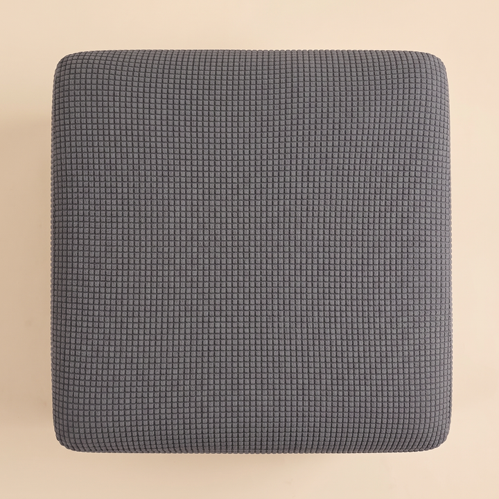 Stretch Ottoman Cover in Charcoal – top-down view of the cover on a plain peach background