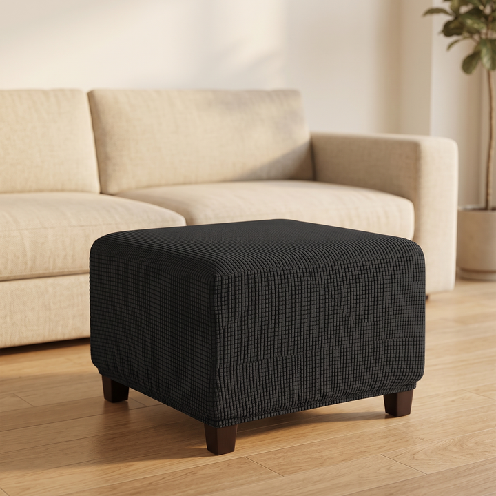 Stretch Ottoman Cover in Black – on an ottoman in front of a cream sofa in a sunlit living room