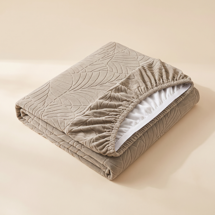 Stretch Couch Cushion Cover – Leaf Jacquard in Beige – folded on a plain surface with elastic hem and white lining visible