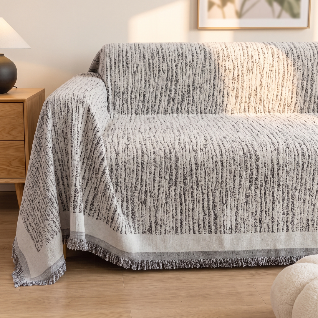 Striped Chenille Couch Cover with Fringe in Gray Stripe – spread across sofa seat and back beside fluffy pouf