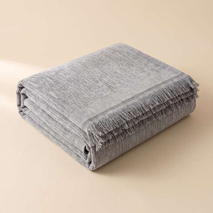 Striped Chenille Couch Cover with Fringe in Gray – folded in a neat stack on a plain beige background