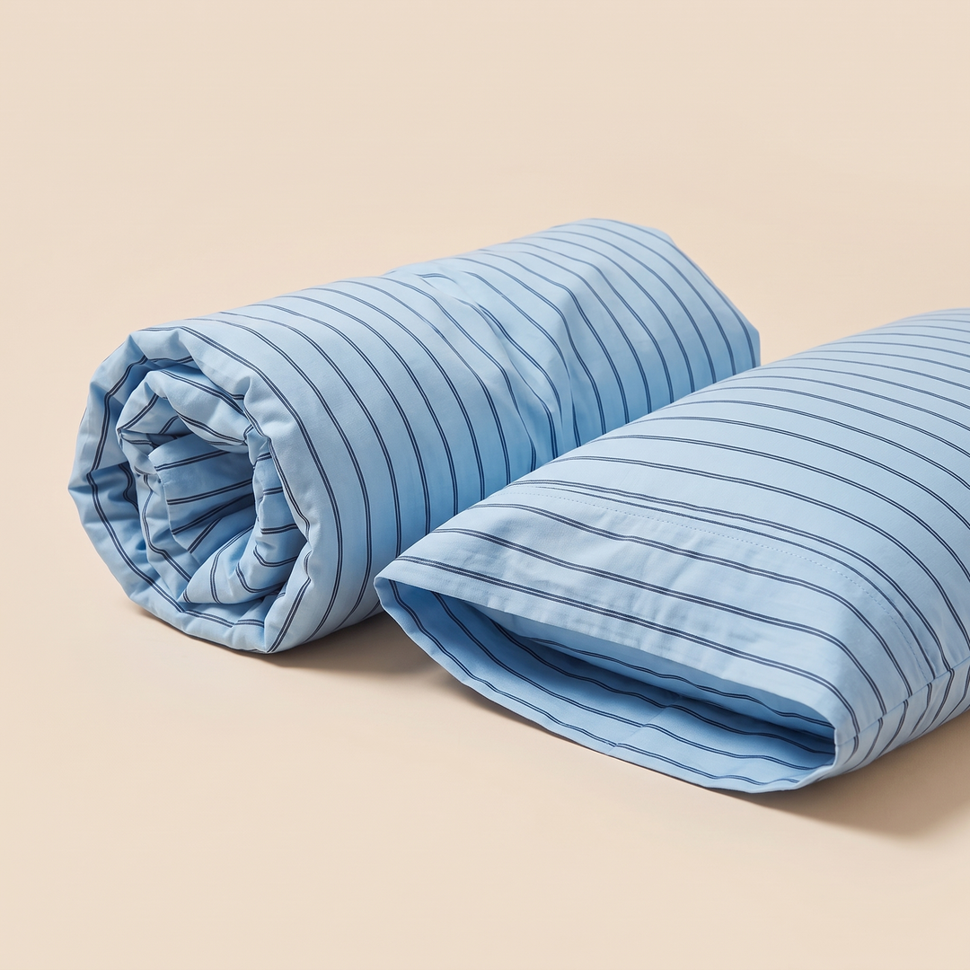 Striped Cotton Pillowcases – Set of 2 in Light Blue Stripe – one rolled up beside one open pillowcase on beige