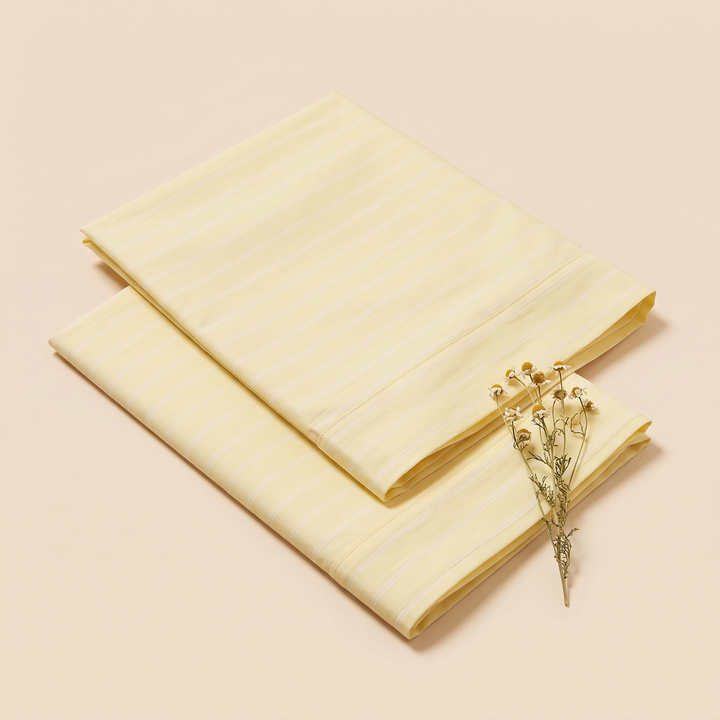 Striped Cotton Pillowcases – Set of 2 in Light Yellow Stripe – two folded pillowcases with dried chamomile flowers resting on the corner