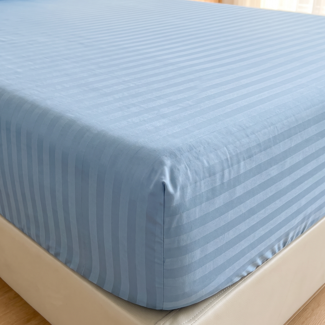 Striped Fitted Sheet – Tone-on-Tone in Blue – close-up of a mattress corner with fitted sheet and wooden floor