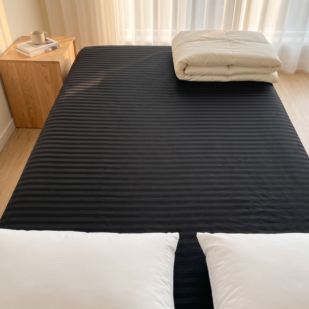 Striped Fitted Sheet – Tone-on-Tone in Black – high angle view with folded duvet and mug-topped nightstand