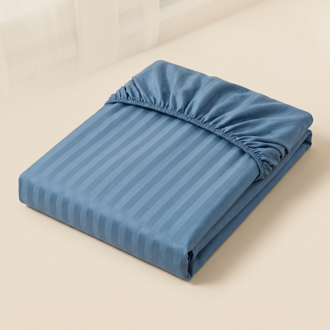 Striped Fitted Sheet – Tone-on-Tone in Blue – folded neatly with elastic edge visible on a plain cream surface