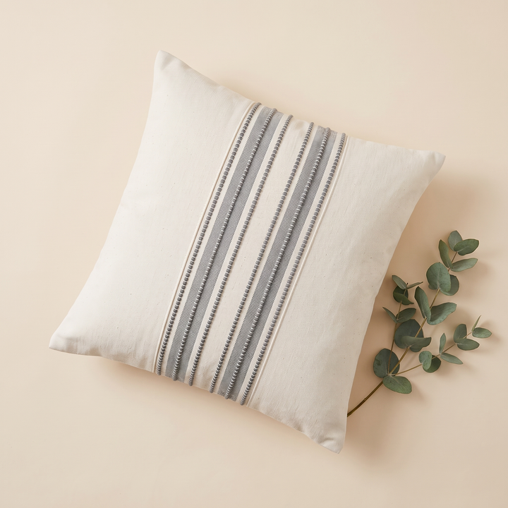 Striped Throw Pillow Cover in Gray Stripe – flat lay on a peach surface with an eucalyptus sprig beside it