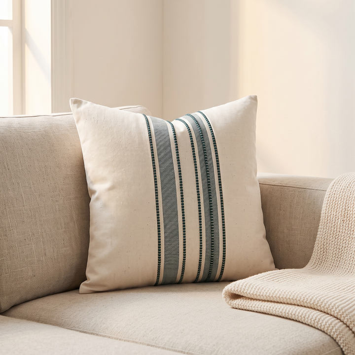 Striped Throw Pillow Cover in Teal Stripe – propped in the corner of a beige sofa beside a knit blanket