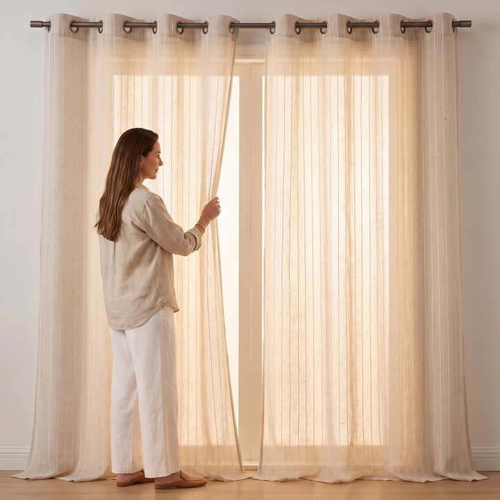 Striped Sheer Curtain Panel – Linen Look in Oat – woman in linen outfit pulling one panel aside at a sunlit window