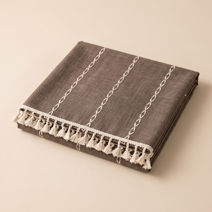 Striped Tassel Tablecloth – Linen Look in Taupe Stripe – folded neatly on a plain beige background, tassels along front edge