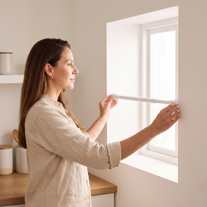Tension Curtain Rod – No Drill in White – woman installing it inside a window recess by hand
