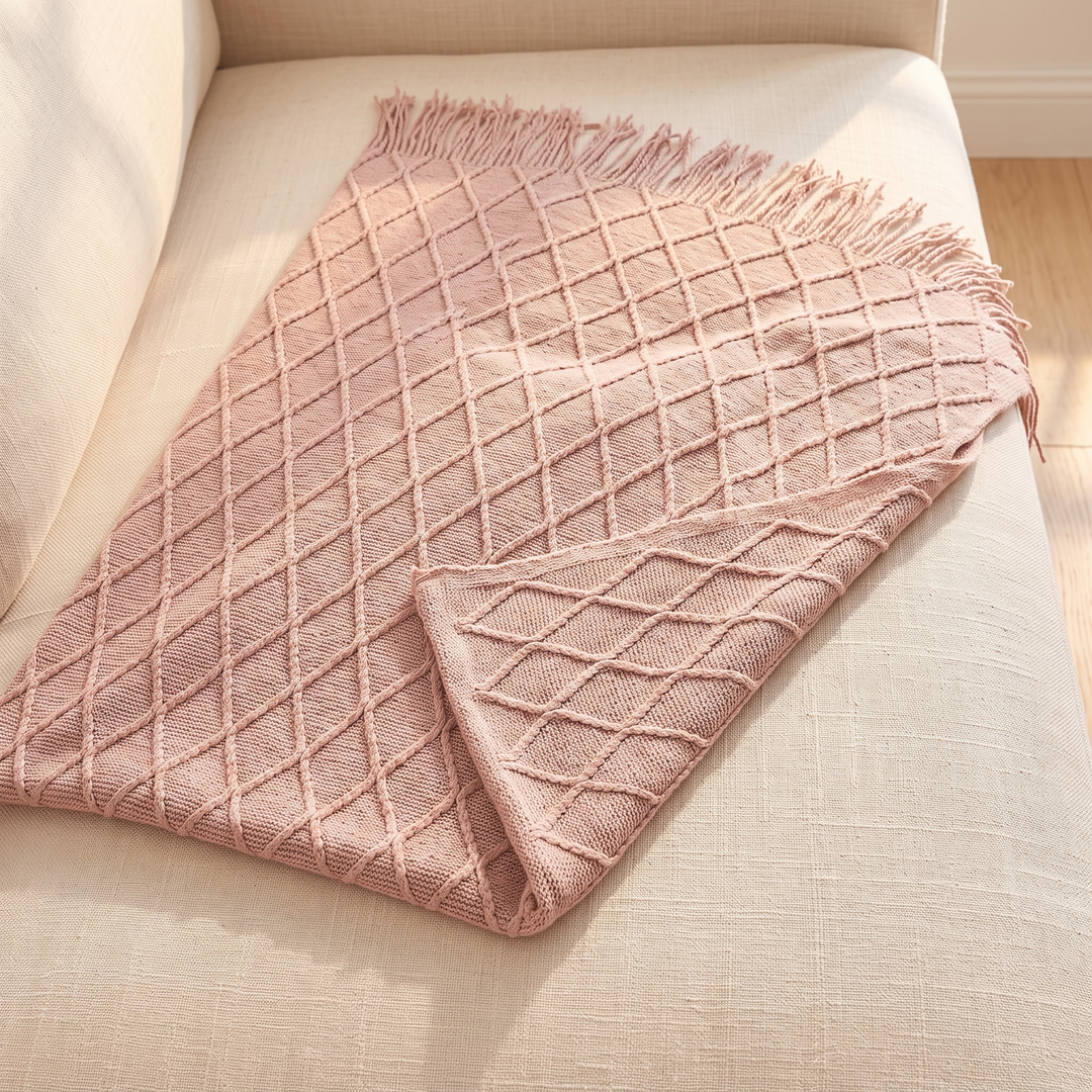 Knit Throw Blanket with Fringe in Dusty Pink Diamond – laid flat with a turned-back corner on sofa cushion