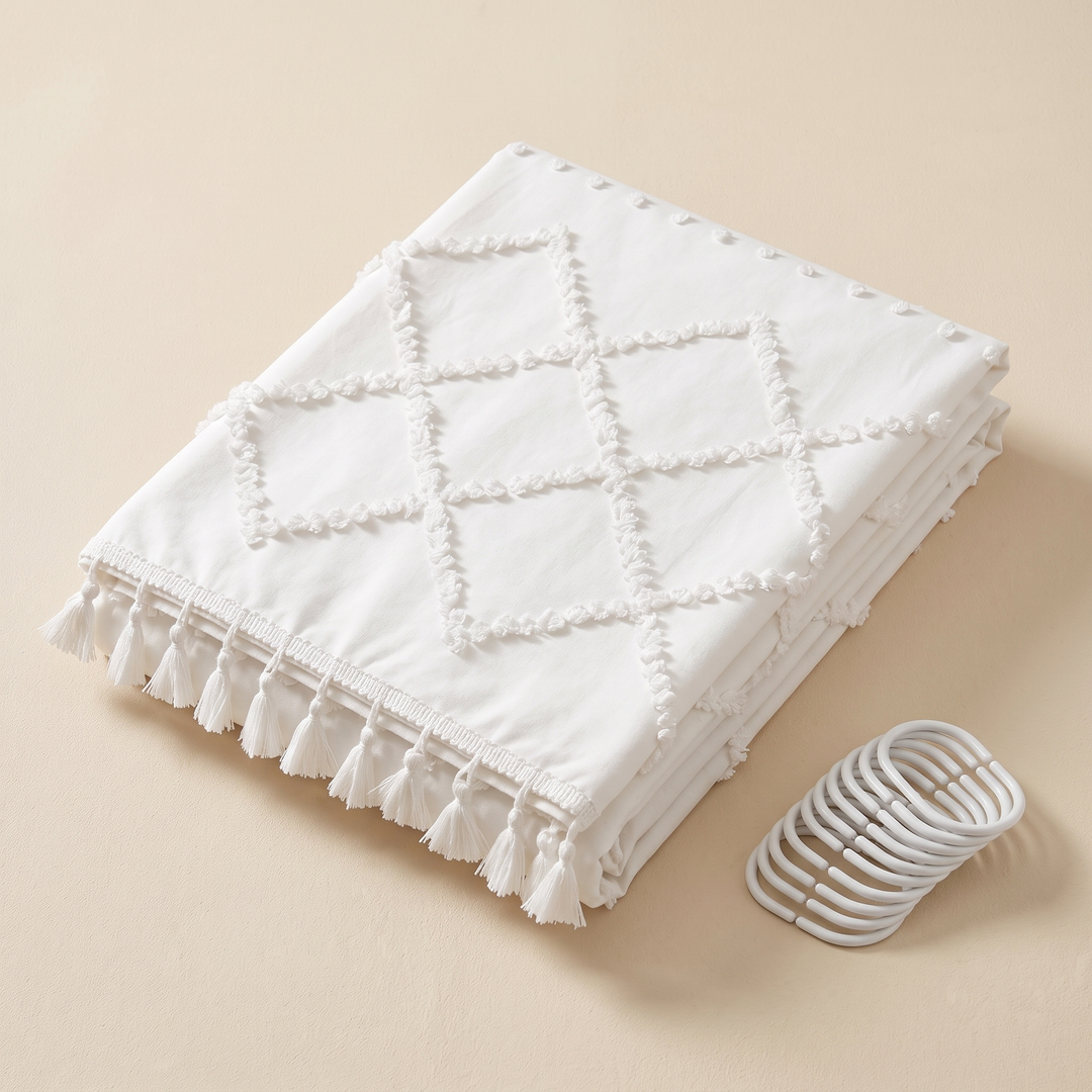 Boho Fabric Shower Curtain – Tufted, with Tassels in White Diamond – folded on a beige surface with a set of shower curtain rings