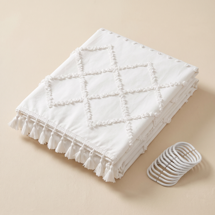 Boho Fabric Shower Curtain – Tufted, with Tassels in White Diamond – folded on a beige surface with a set of shower curtain rings