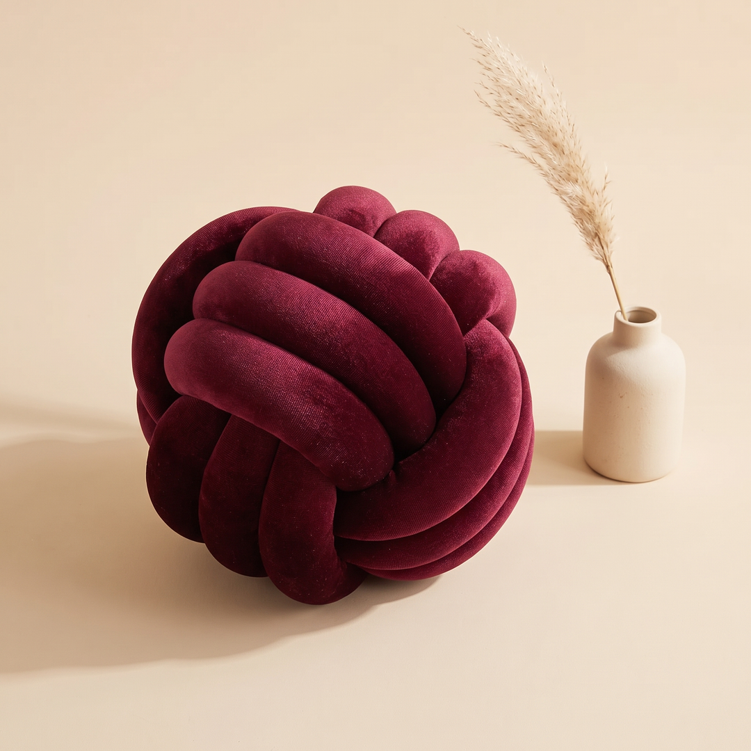 Velvet Knot Pillow in Burgundy – beside a small cream vase with dried pampas grass