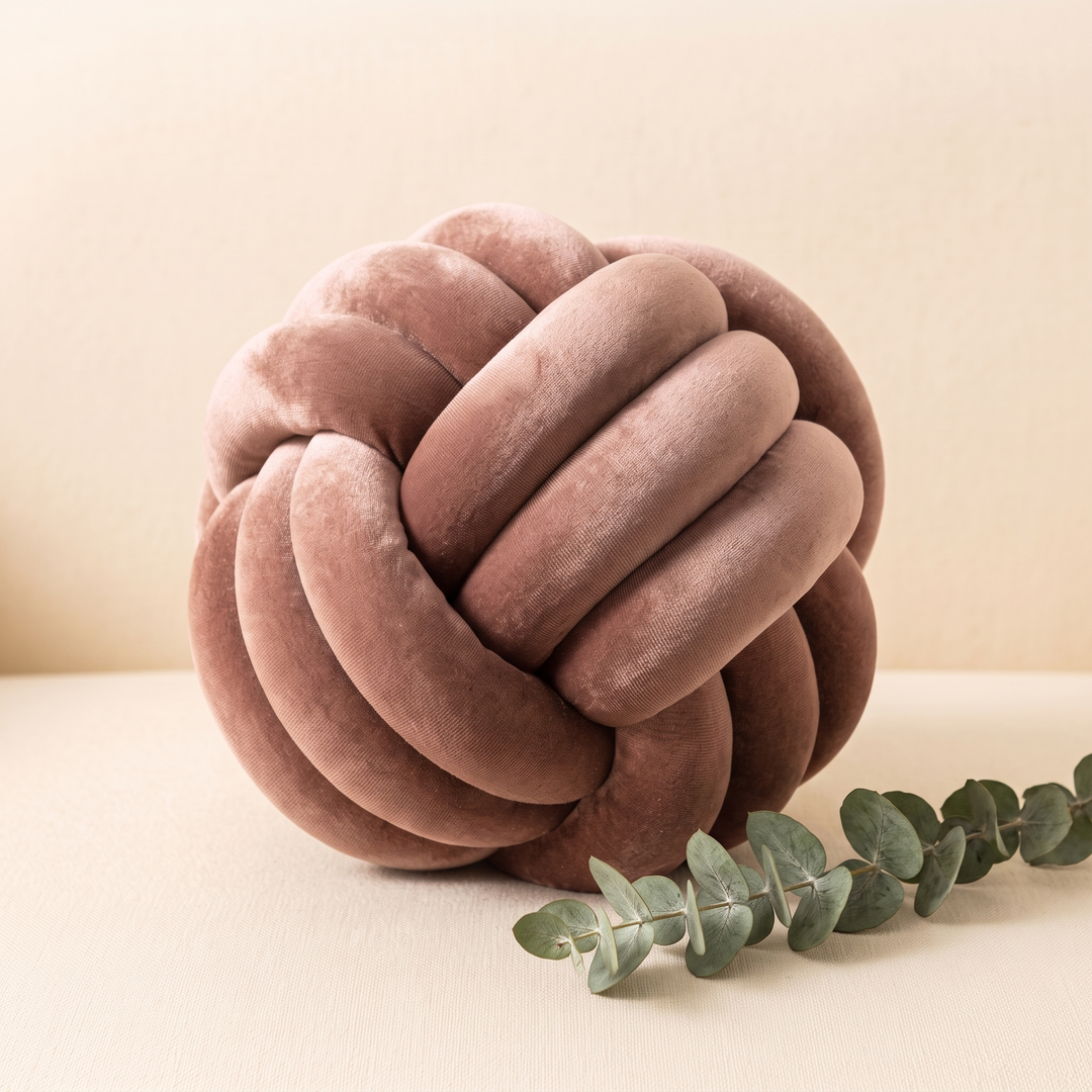Velvet Knot Pillow in Dusty Pink – beside a eucalyptus sprig on a cream surface