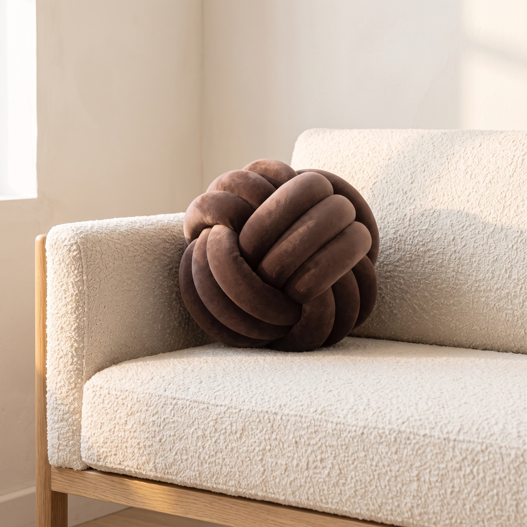 Velvet Knot Pillow in Chocolate Brown – resting on a cream boucle sofa beside a wooden frame