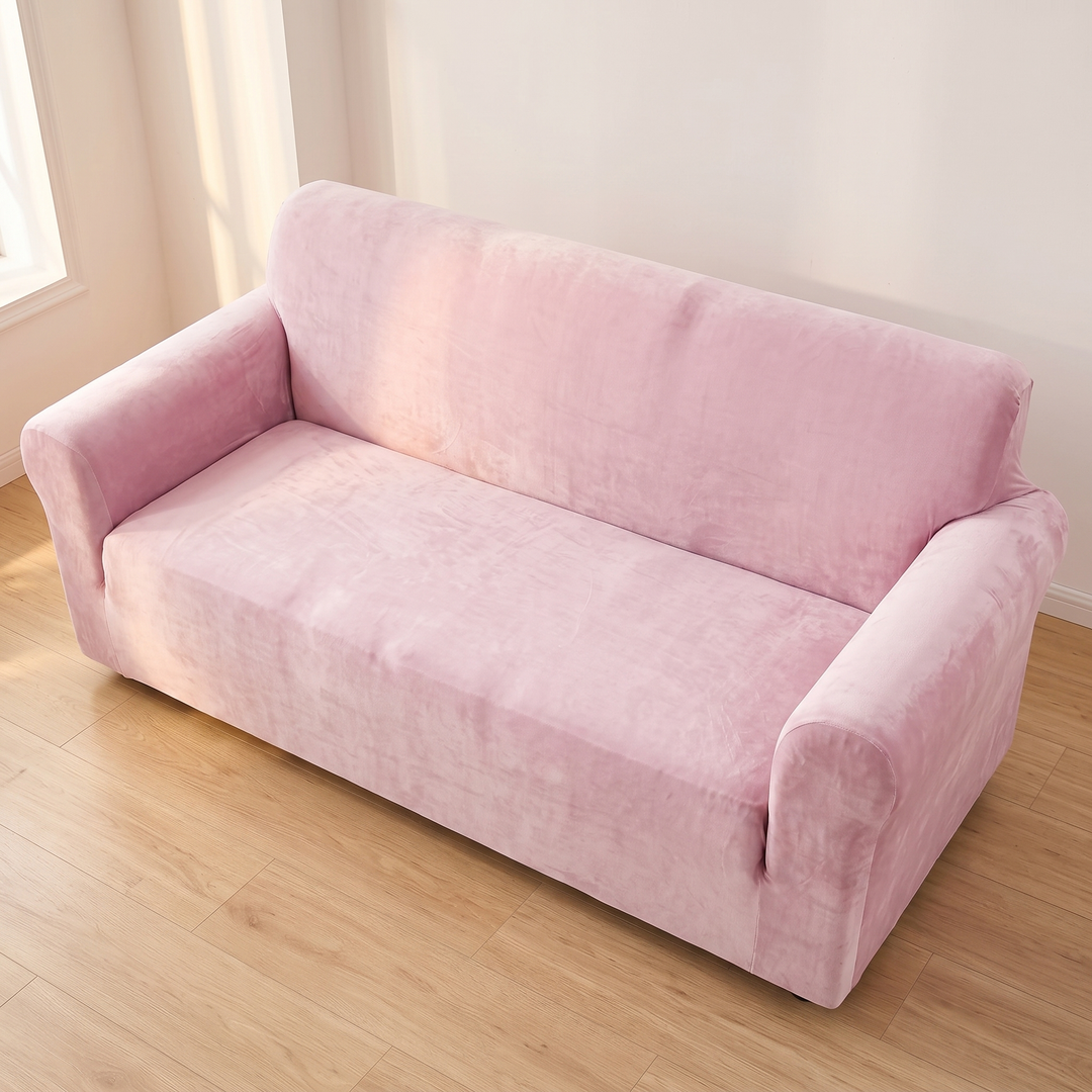 Velvet Stretch Sofa Cover in Light Pink – high angle view against a bare wall with sunlit floorboards