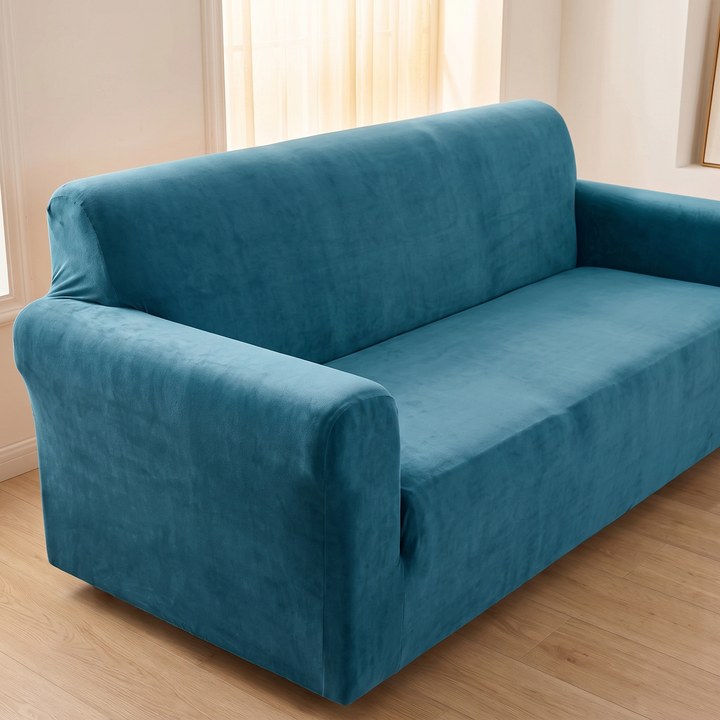 Velvet Stretch Sofa Cover in Teal – raised side angle of empty sofa below a sheer-curtained window