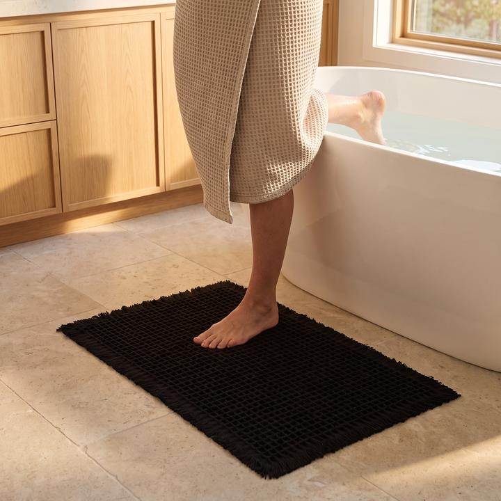 Waffle Bath Mat with Tassels in Black – under a barefoot person stepping into a bathtub