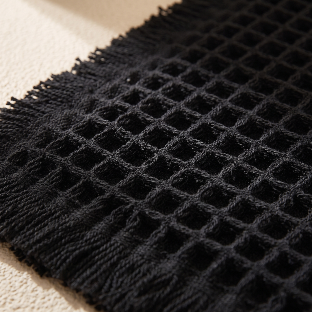 Waffle Bath Mat with Tassels in Black – close-up of the waffle texture and fringed edge on a cream surface