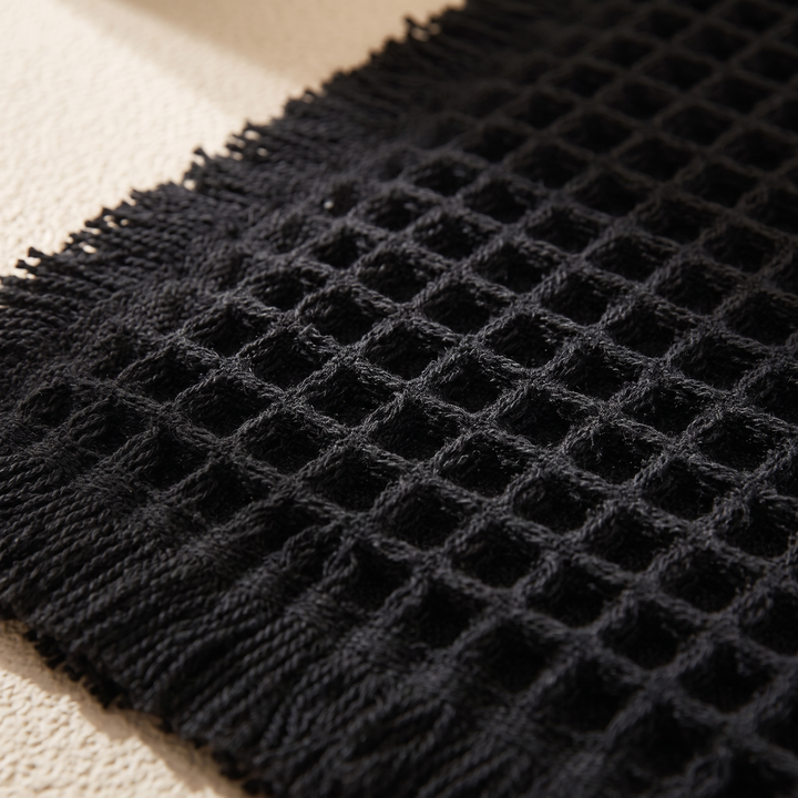 Waffle Bath Mat with Tassels in Black – close-up of the waffle texture and fringed edge on a cream surface