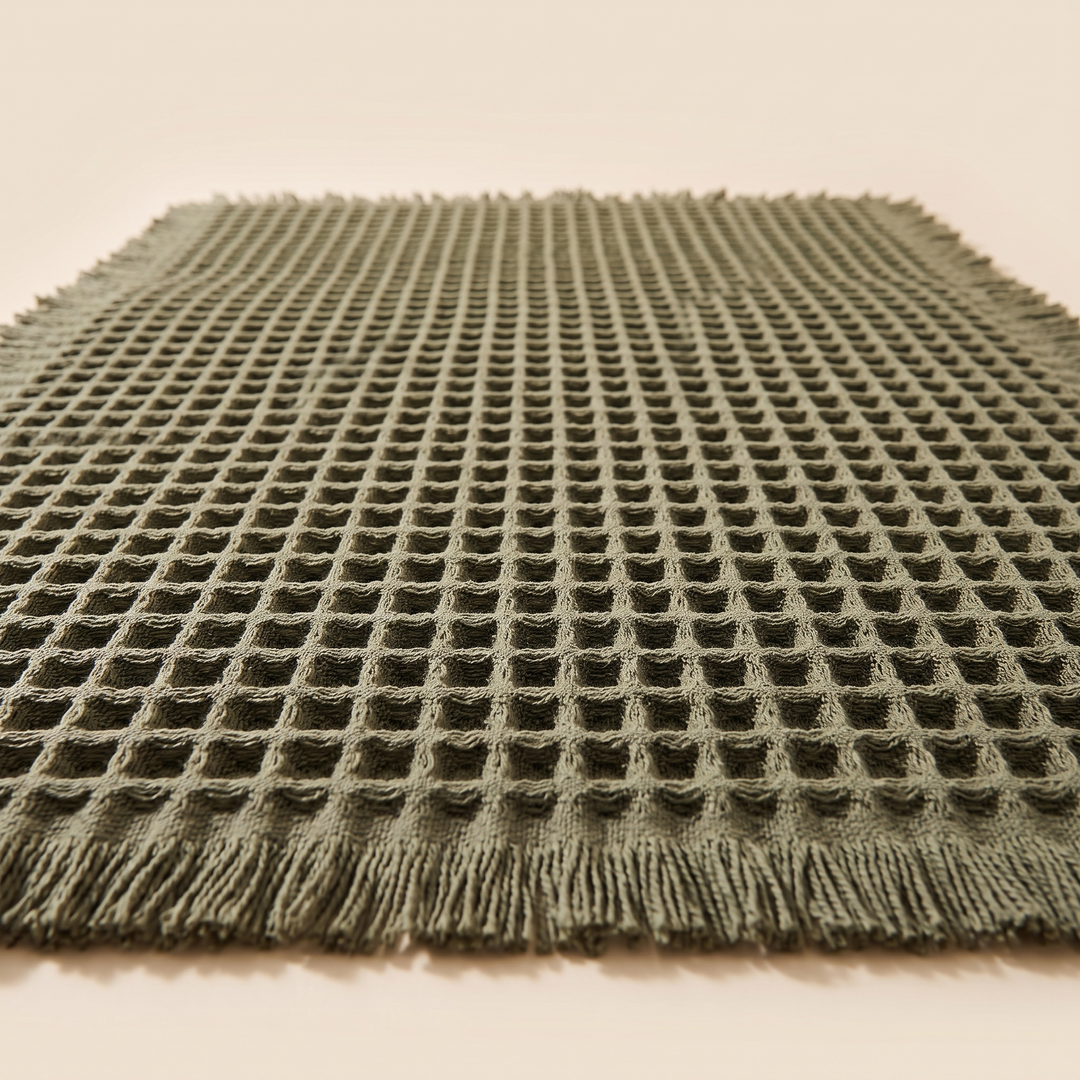 Waffle Bath Mat with Tassels in Olive Green – ground-level view of the waffle grid fading into soft focus