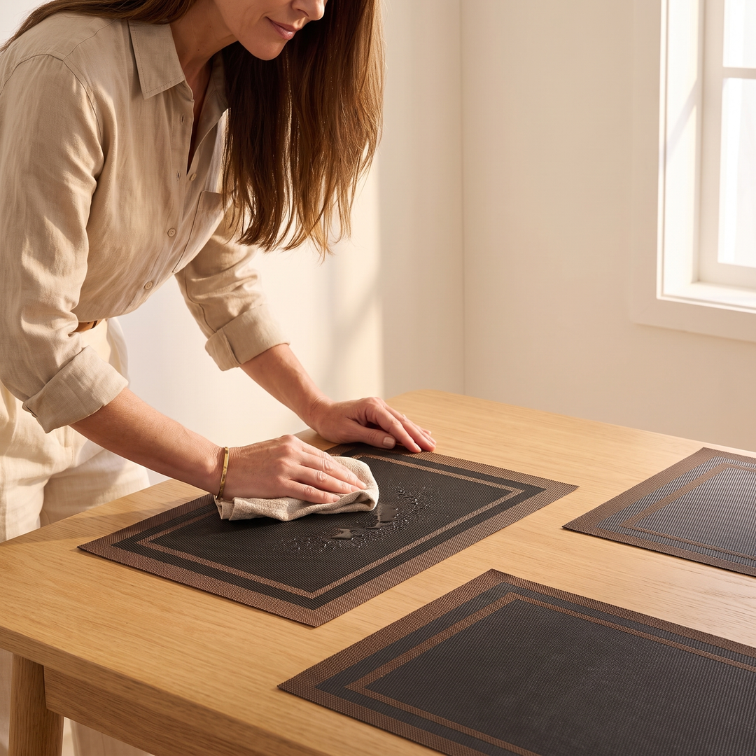 Woven Placemats – Wipe Clean in Black – Frame – being wiped with a cloth on an oak table