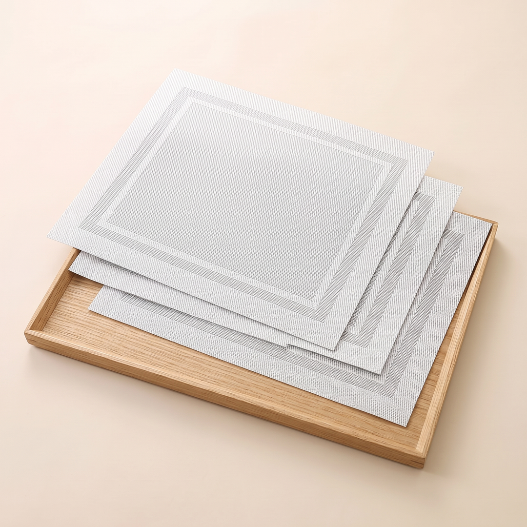 Woven Placemats – Wipe Clean in White – Frame – stacked on a light wooden tray, angled view from above