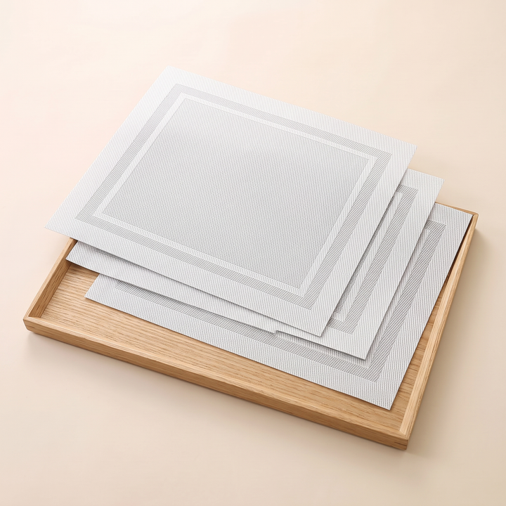 Woven Placemats – Wipe Clean in White – Frame – stacked on a light wooden tray, angled view from above
