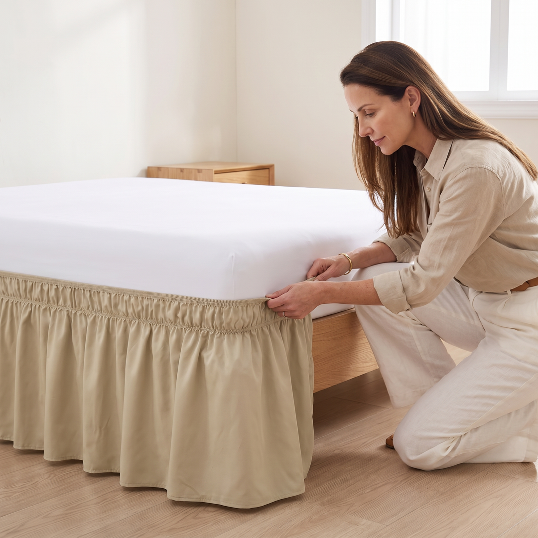 Wrap-Around Ruffled Bed Skirt in Beige – being fitted by a kneeling woman around a bed&