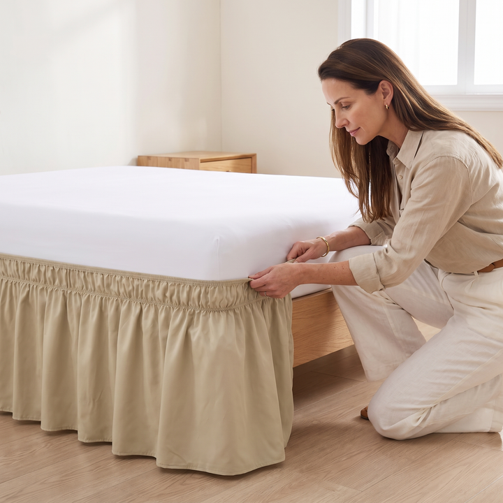 Wrap-Around Ruffled Bed Skirt in Beige – being fitted by a kneeling woman around a bed&